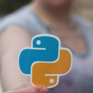 Person holding Python logo sticker with blurred background, highlighting programming focus.