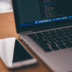 Coding setup with laptop displaying code and smartphone on a wooden table, ideal for tech themes.