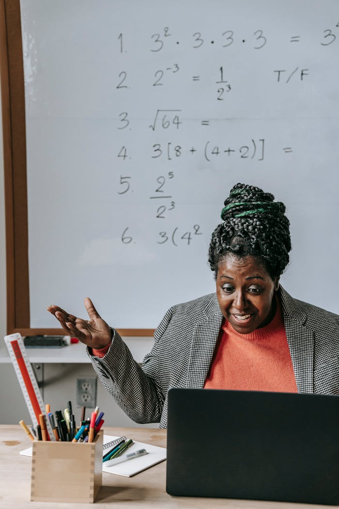 Positive smart African American female tutoring online with netbook in classroom with whiteboard