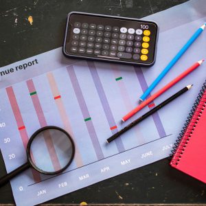 Flat lay of revenue report with a calculator, pencils, and notebook.